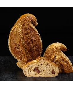 Rustikales Schinken-Sauerkraut-Brot mit dunkler Kruste und Sesam, kunstvoll geformt und angeschnitten auf dunklem Untergrund.