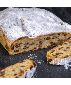 Traditioneller Chris-Stollen als Rosinenstollen mit Puderzucker und saftigen Rosinen, angeschnitten auf dunklem Untergrund.