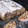 Frischer Cranberry-Stollen mit hellerer Krume, roten Cranberry-Stückchen und Puderzucker, angeschnitten auf dunklem Untergrund.