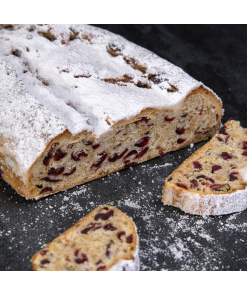 Frischer Cranberry-Stollen mit hellerer Krume, roten Cranberry-Stückchen und Puderzucker, angeschnitten auf dunklem Untergrund.