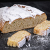 Traditioneller Mandelstollen mit heller Krume und Puderzucker, angeschnitten und auf dunkler Fläche angerichtet.