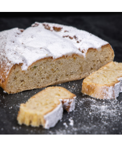 Traditioneller Mandelstollen mit heller Krume und Puderzucker, angeschnitten und auf dunkler Fläche angerichtet.